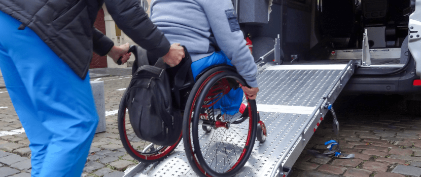 Nurse pushing patient in wheelchair up ramp into a car